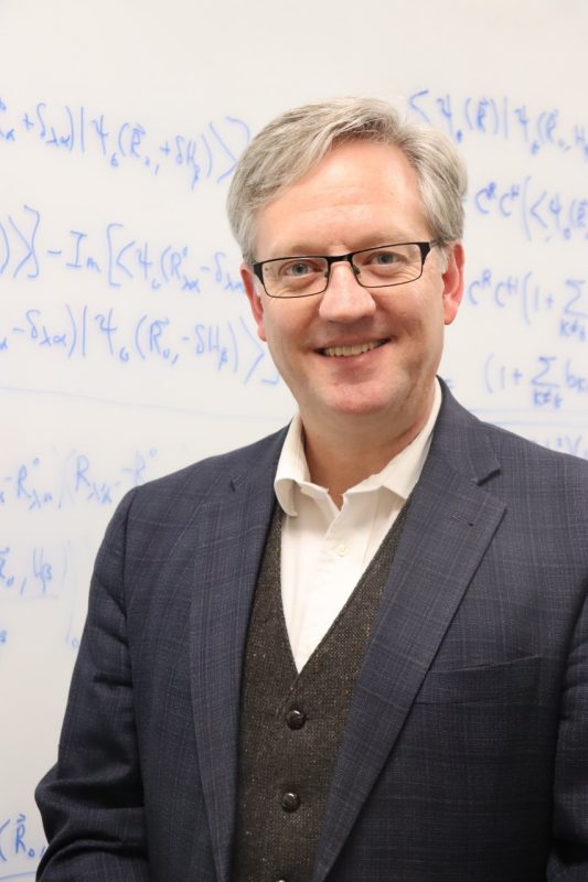 Portrait of Professor Daniel Crawford in front of a whiteboard full of equations